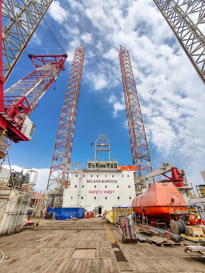Oil rig platform with cranes and safety message under clear blue sky.