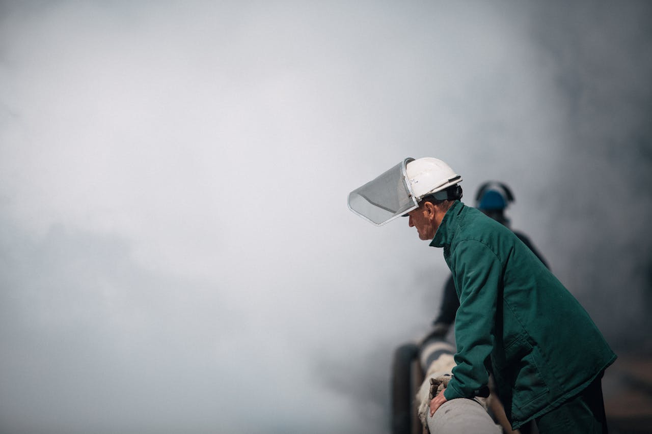 services-02 Industrial worker in protective gear inspecting a large pipe amidst dense smoke in an outdoor setting.